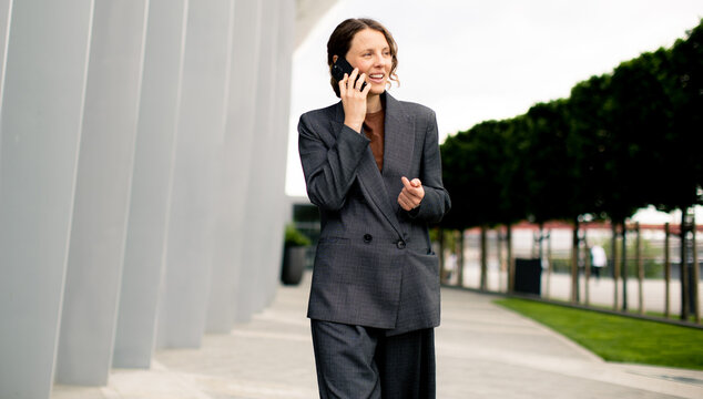Business woman walks and talks on phone outside modern building in city