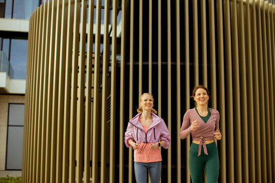 Two women running together outside a modern building in bright daylight