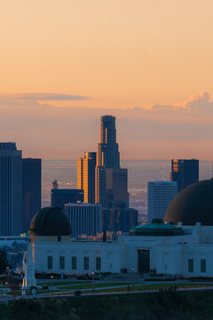 View of Griffith Observatory with the Los Angeles skyline in the background during golden hour, featuring the iconic dome and historic architecture in Los Angeles, California, United States.