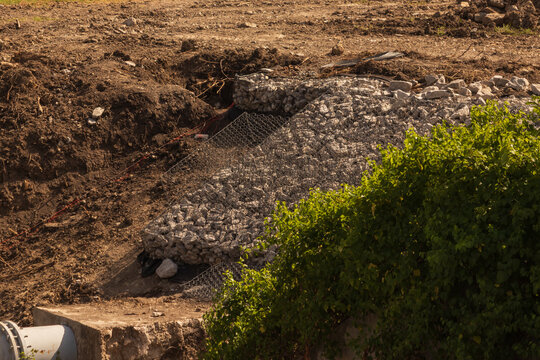 Wire mesh retaining cages filled with stones for soil erosion control on a construction site embankment