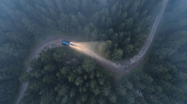 Aerial top view of a winding road through a foggy forest with a car driving at night, glowing headlights illuminating the mist, cinematic natural landscape