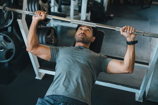 Man, bench press, barbell, gym, workout, strength exercise with focused male athlete lifting weight on indoor fitness equipment for chest training