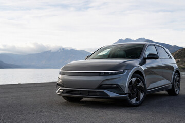 Obraz premium Gray electric vehicle parked on asphalt road with mountain backdrop