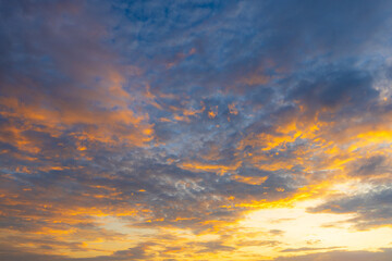 Fototapeta premium Dramatic Golden Sunset Sky with Vibrant Clouds,A breathtaking view of a dramatic golden sunset sky, filled with vibrant orange and yellow clouds scattered across a deep blue twilight atmosphere,