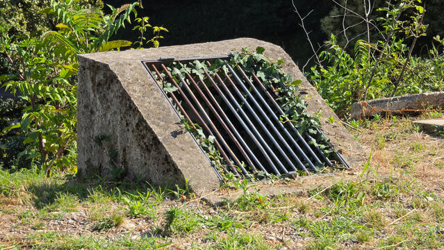 Angled concrete headwall culvert with parallel iron safety bars on grassy terrain
