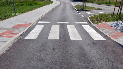 White zebra crossing painted on a fresh asphalt road between paved sidewalks © hecos