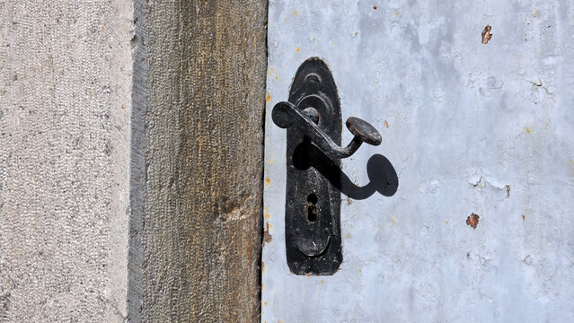 Vintage black wrought iron door handle and backplate on a weathered metal door