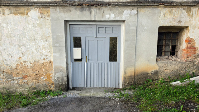 Weathered historic plaster wall with a gray wood door and barred basement window