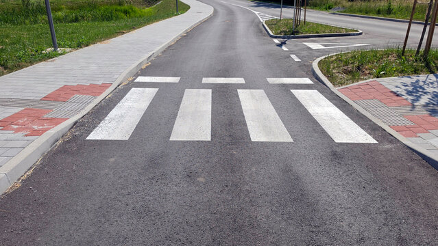 White zebra crossing painted on a fresh asphalt road between paved sidewalks