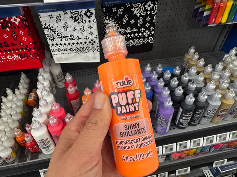 Mesa, Arizona - June 27, 2026: Hand holds a bottle of Tulip puff paint in fluorescent orange color at a craft store
