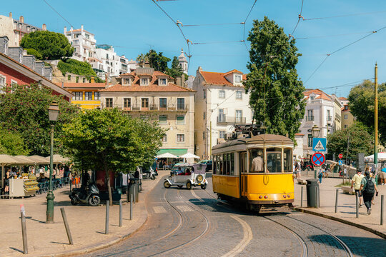 Yellow tram navigating a lisbon street with historic buildings and people