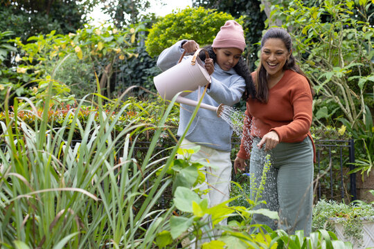 African mother and child standing in home garden, watering plants with pale pink watering can