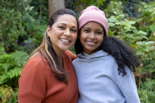 African American mother and teenage daughter smiling in garden wearing pink beanie and rust sweater