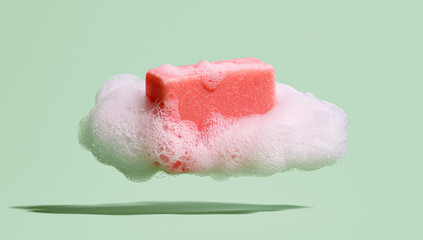 Fototapeta premium Minimal skincare concept featuring a floating pink soap bar surrounded by soft white foam on a pastel green background.