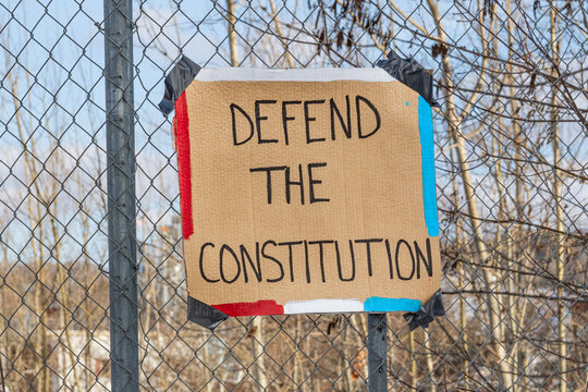 Homemade sign taped to fence reading "Defend the Constitution"