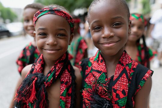 Two young girls smile warmly at the camera. They wear vibrant red and green traditional garments. Their headbands match their colorful attire. Bright smiles convey joy and cultural pride