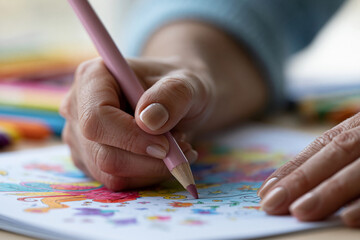 Naklejka premium Soft pink pencil draws vibrant colors on paper. Hands gently color a whimsical, detailed design. Calm focus suggests creativity, patience, and joy. Perfect for educational, therapeutic