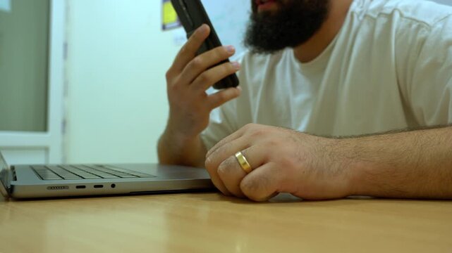Businessman talking on a smartphone while working at an office desk with a laptop nearby. Modern business communication, remote work and mobile technology in an office.