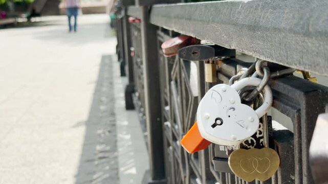 Heart padlocks are locked tightly onto a bridge railing next to a public path. They show eternal romance, joyful devotion, and deep affection shared by couples.