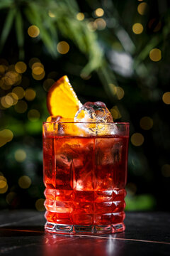Zero proof negroni mocktail non alcoholic cocktail drink with clear ice cube. Extreme close up portrait framing featuring rich crimson beverage color and bright sparkles.