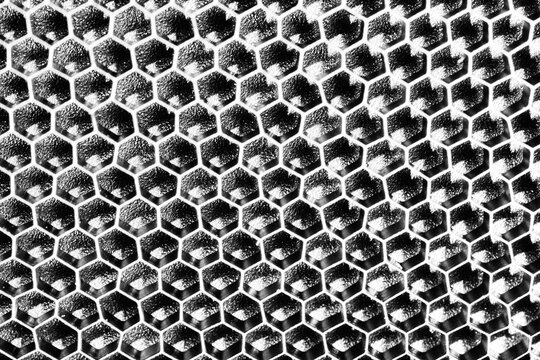 Monochrome macro shot of a shallow aluminum hexagonal grid against a shiny black backdrop