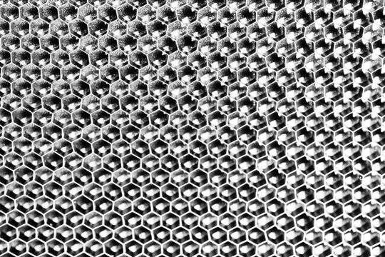 Monochrome macro shot of a shallow aluminum hexagonal grid against a shiny black backdrop