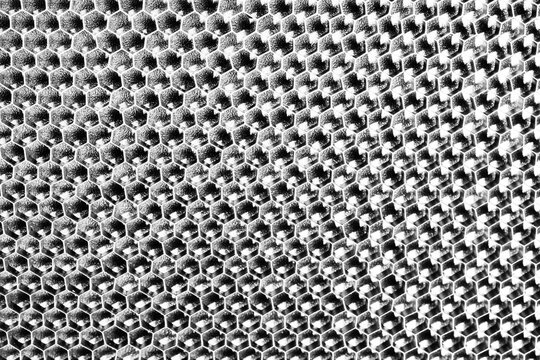 Monochrome macro shot of a shallow aluminum hexagonal grid against a shiny black backdrop
