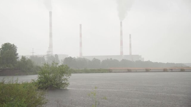 industrial landscape with foggy day and stationary view of smokestacks and water bodies at an urban development site, muted and industrial mood, concrete structures and metal poles visible.