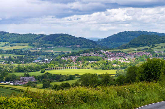 Scenic overlook of Monmouth, Wales, featuring lush green fields, rolling hills, and a tranquil rural town stretching into the distance.