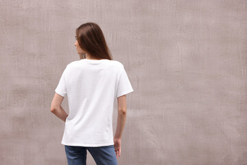 Obraz premium Woman wearing stylish white t-shirt near grey wall outdoors, back view. Space for text