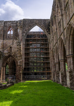 Tintern Abbey, a historic ruin in Wales, showcases ancient stone arches and a prominent scaffolding structure in its interior.
