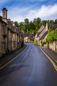 Historic village street scene in Castle Combe, Wiltshire, England. Traditional stone homes line a curved road.
