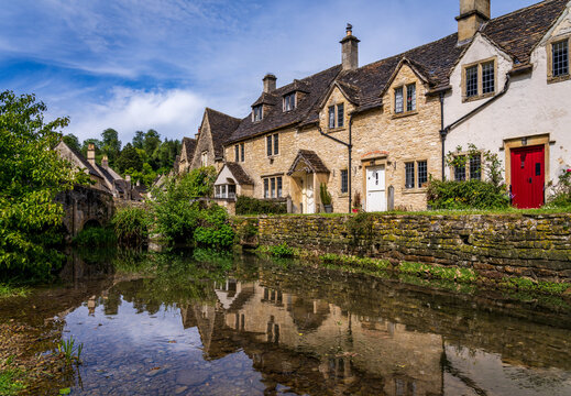 Historic Weavers Cottages reflecting in the River Bybrook, Castle Combe, Wiltshire, England on a clear day.