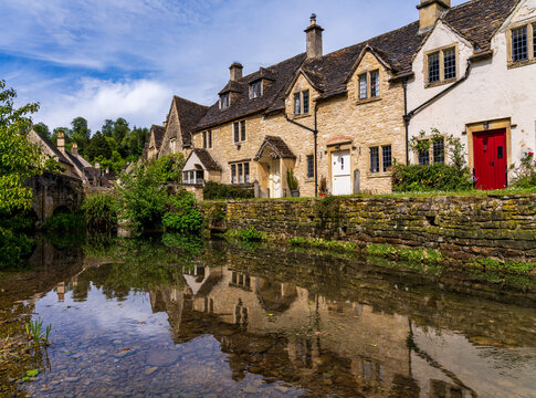 Historic Weavers Cottages reflecting in the River Bybrook, Castle Combe, Wiltshire, England on a clear day.