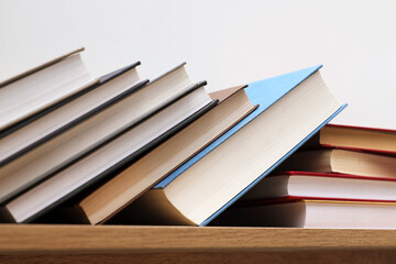 Fototapeta premium Different books on wooden shelf near white wall indoors, closeup