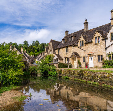 Historic Weavers Cottages reflecting in the River Bybrook, Castle Combe, Wiltshire, England on a clear day.