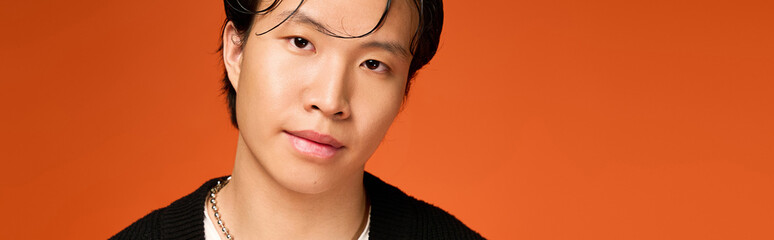 Fototapeta premium Stylish young man showcases modern fashion in vibrant orange studio setting