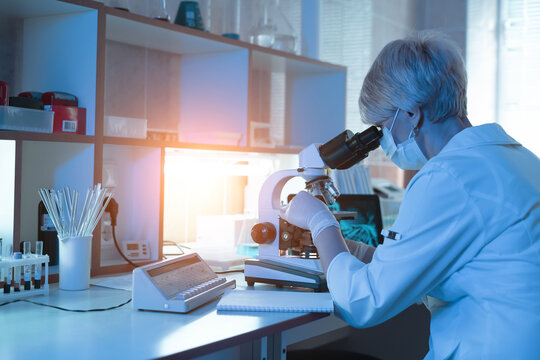 Female medical Doctor or research scientist looking through a microscope in a laboratory.science experiments,laboratory glassware containing chemical liquid for researching biology chemistry samples