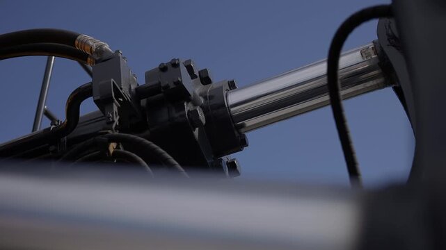 Hydraulic cylinder piston extending on industrial machinery arm against clear blue sky.
