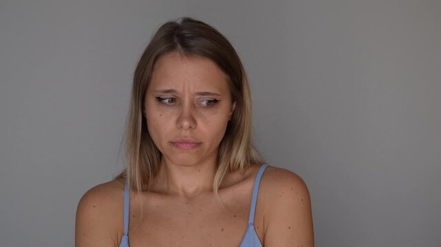 Young blonde woman checks her underarm smell with a disgusted facial expression, showing bad odor, sweat and personal hygiene problem in a relatable body care concept on a grey background