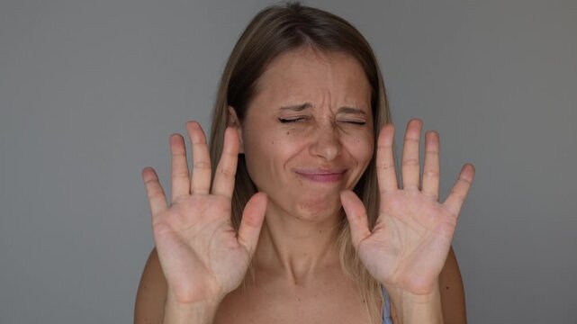 Young blonde woman shows refusal and non-acceptance with expressive hand gestures, saying no-no-no in a clear denial, rejection and disapproval concept on a grey background