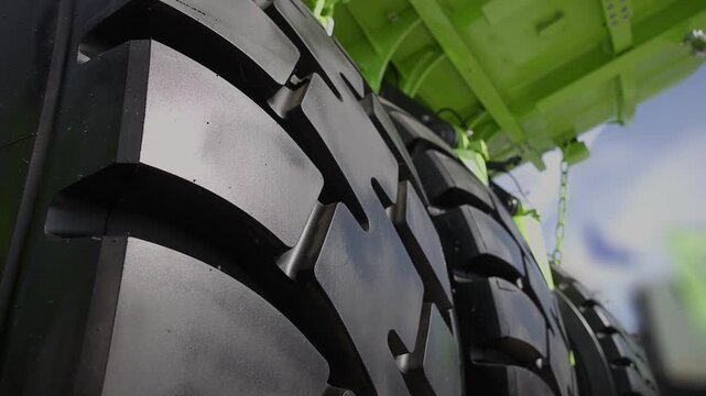Slow motion closeup of tractor tires rotating under green agricultural trailer at low angle tracking shot.