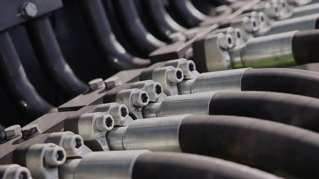 Tracking shot of hydraulic hoses and metal fittings arranged on industrial machinery in factory assembly with shallow focus and gentle pan.