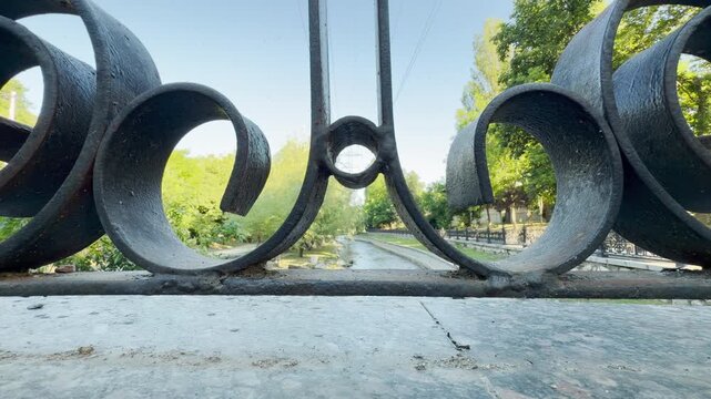 An ornate iron railing frames a peaceful river flowing through a park in Simferopol, Crimea. This beautiful view evokes deep feelings of calm and nostalgic wonder.