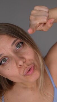 Young blonde woman points at the camera with an accusing expression, blaming someone in a direct and confrontational emotional portrait on a grey background