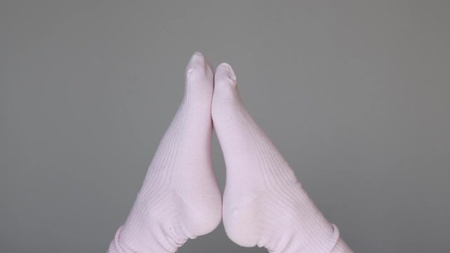 Two feet in pink socks dance like cheerful puppets, creating a playful cozy composition with funny movement and childlike energy on a grey background