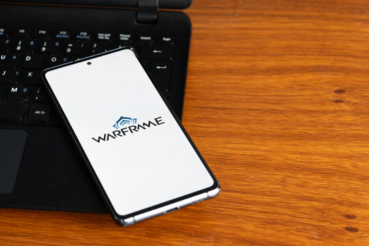 Punta Arenas, Chile &ndash; July 2, 2026: The Warframe logo displayed on a smartphone screen resting on a laptop keyboard over a wooden table background