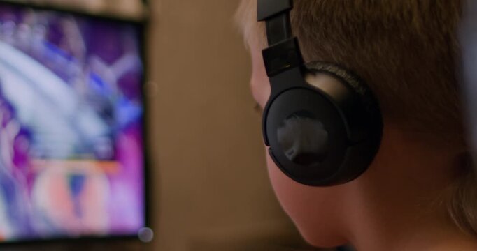 A boy sits in front of a monitor, wearing headphones, playing an eSports game on a computer. Childhood addiction to computer games.