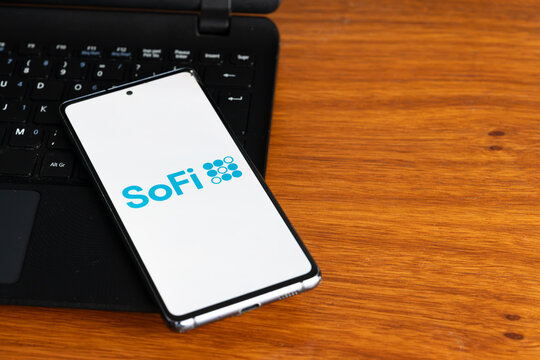 Punta Arenas, Chile &ndash; July 2, 2026: The SoFi logo displayed on a smartphone screen resting on a laptop keyboard over a wooden table background