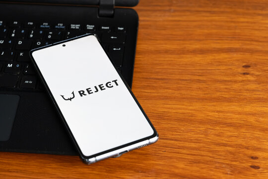 Punta Arenas, Chile &ndash; July 2, 2026: The REJECT esports organization logo displayed on a smartphone screen resting on a laptop keyboard over a wooden table background